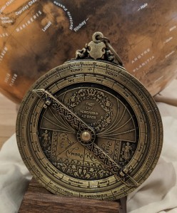 A brass astrolabe. In the background is a globe of Mars.